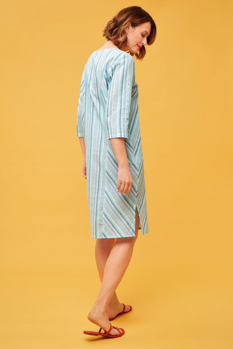 Lily Ella Collection light blue and white striped midi dress with three-quarter sleeves and side slit, paired with red sandals on warm yellow background.