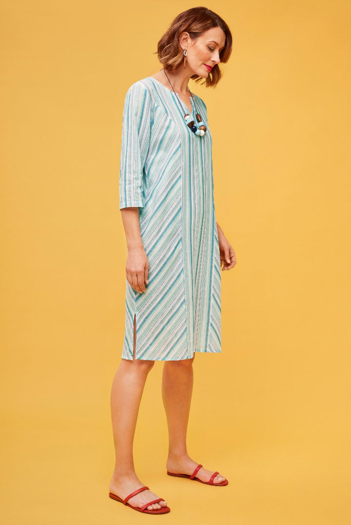 Lily Ella Collection mint green and white striped dress, casual summer midi dress with three-quarter sleeves and v-neck, styled with red sandals and statement necklace, on warm yellow background.