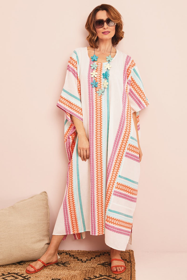 Lily Ella Collection bohemian style white maxi dress with pink and turquoise pattern, stylish summer outfit, model wearing sunglasses and coral sandals, accessorized with floral necklace.