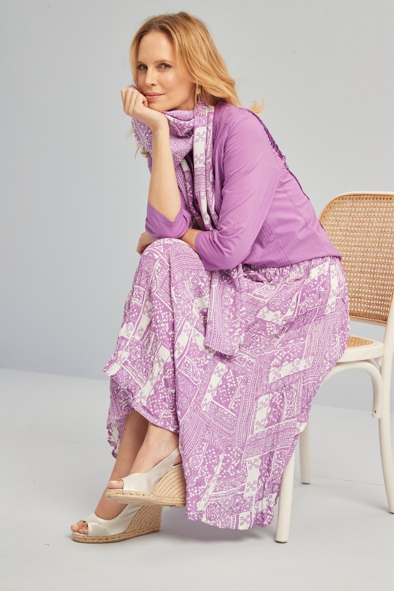 Lily Ella Collection stylish purple patterned skirt and matching scarf, elegant woman sitting on chair, casual chic summer outfit, comfortable wedge sandals, fashion photoshoot.