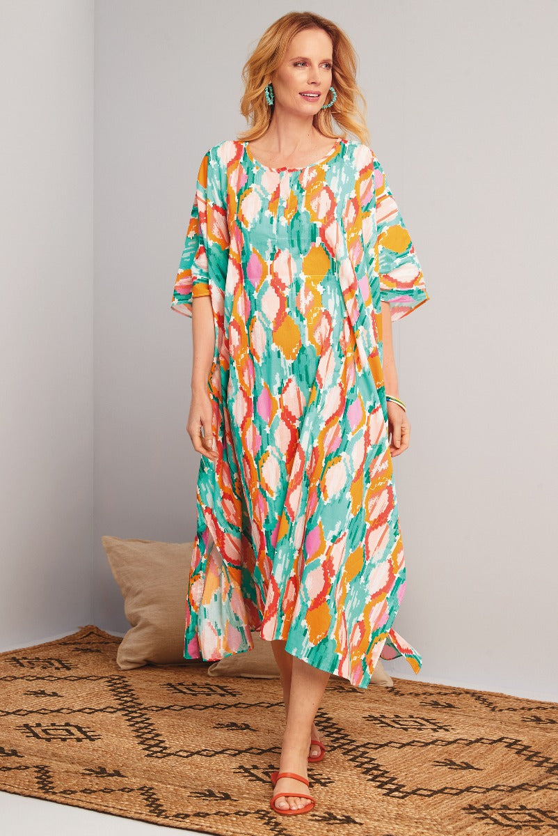Lily Ella Collection vibrant multi-color abstract print midi dress, stylish comfortable women's summer fashion, teal orange pink patterned dress with three-quarter sleeves and side slits, paired with teal earrings and orange sandals.