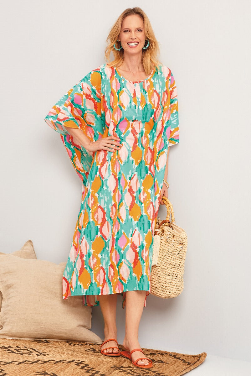 Lily Ella Collection vibrant green, orange, and pink patterned kaftan dress with smiling model holding a straw bag and wearing matching sandals.
