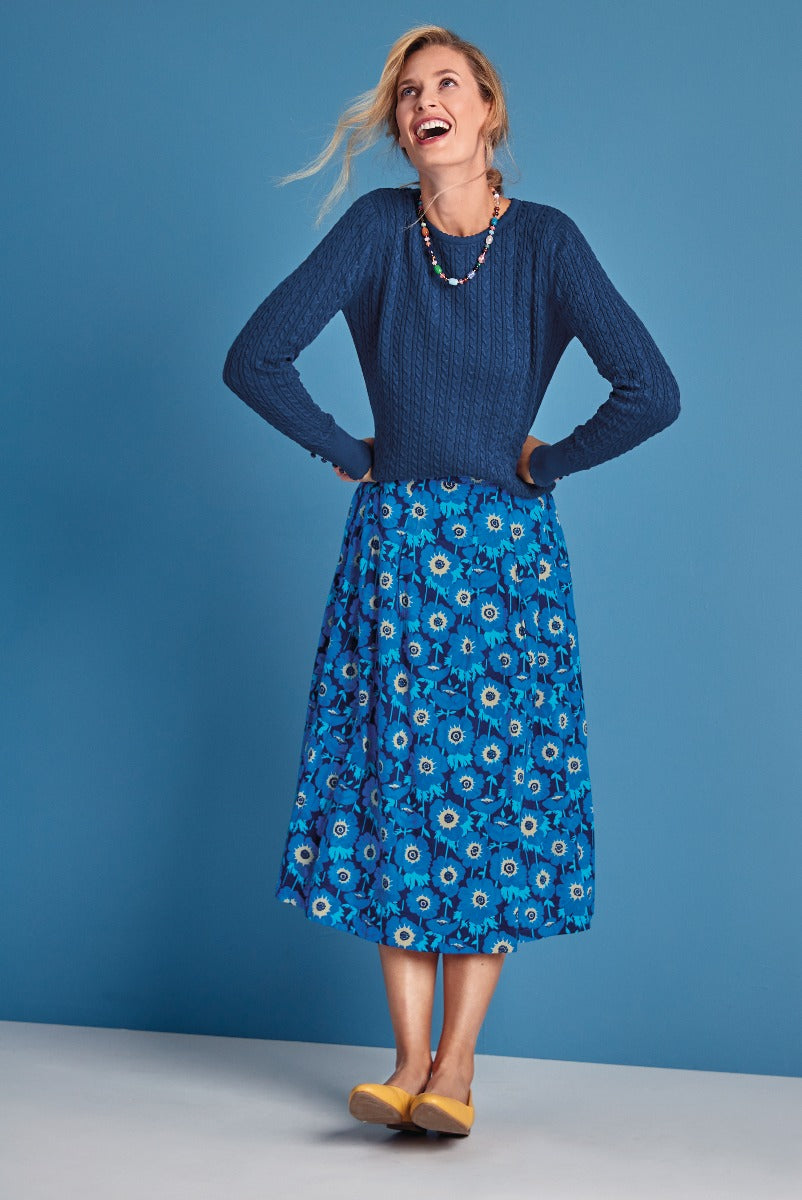 Lily Ella Collection stylish woman in blue cable knit sweater and floral patterned blue A-line skirt with mustard yellow shoes, fashion-forward casual wear, cheerful and elegant outfit.