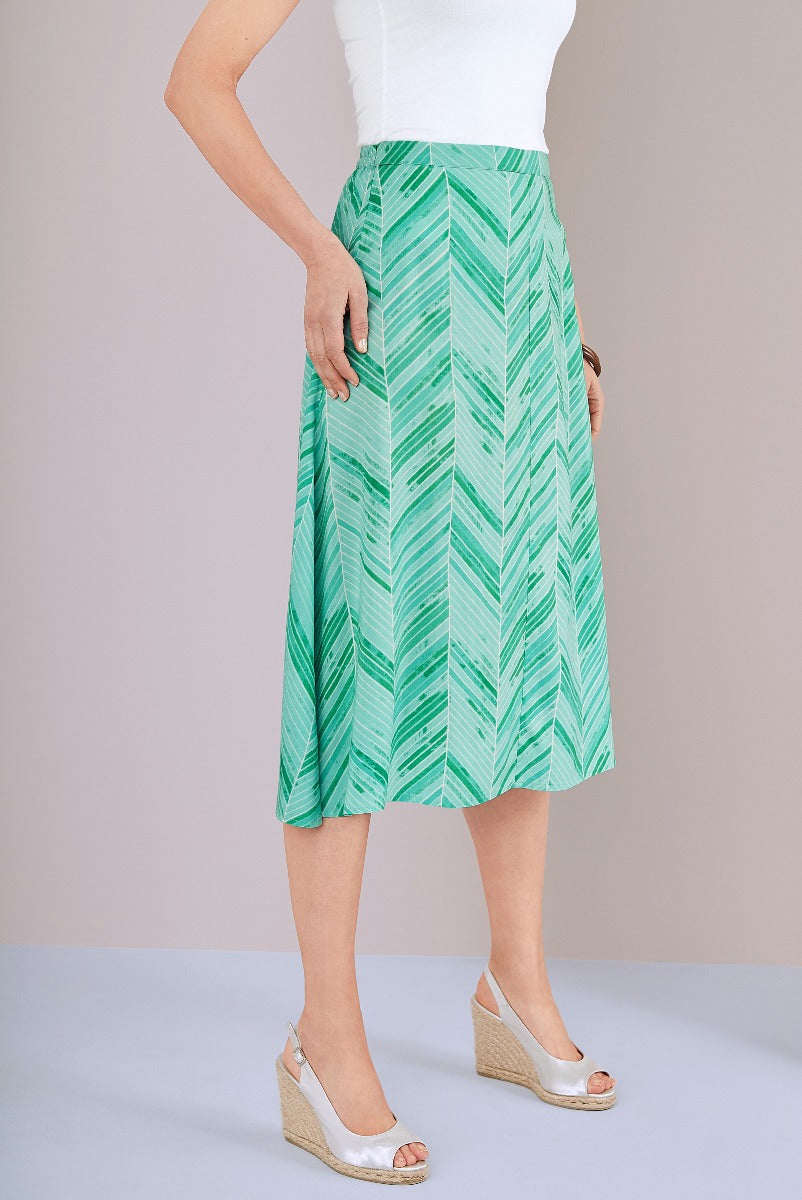 Lily Ella Collection green leaf print pleated midi skirt paired with white top and beige wedge sandals for a spring-summer look.