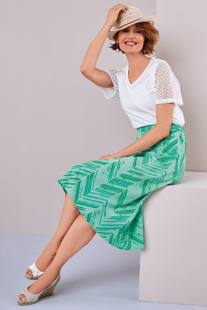Lily Ella Collection summer look featuring white crochet detail top with striped green midi skirt, stylish straw hat, and white wedge sandals for sophisticated casual fashion.