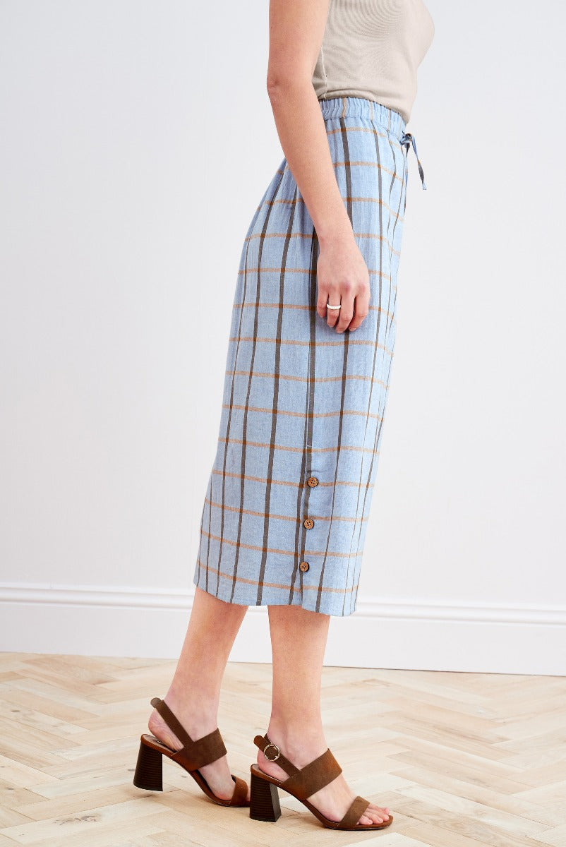 Lily Ella Collection blue plaid midi skirt with button detail and beige drawstring top paired with brown leather block heel sandals for a casual spring look