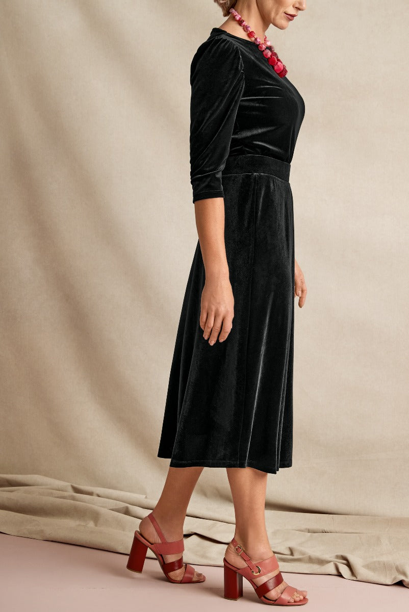 Lily Ella Collection elegant black velvet midi dress with three-quarter sleeves and cinched waist paired with red block heel sandals and statement necklace.