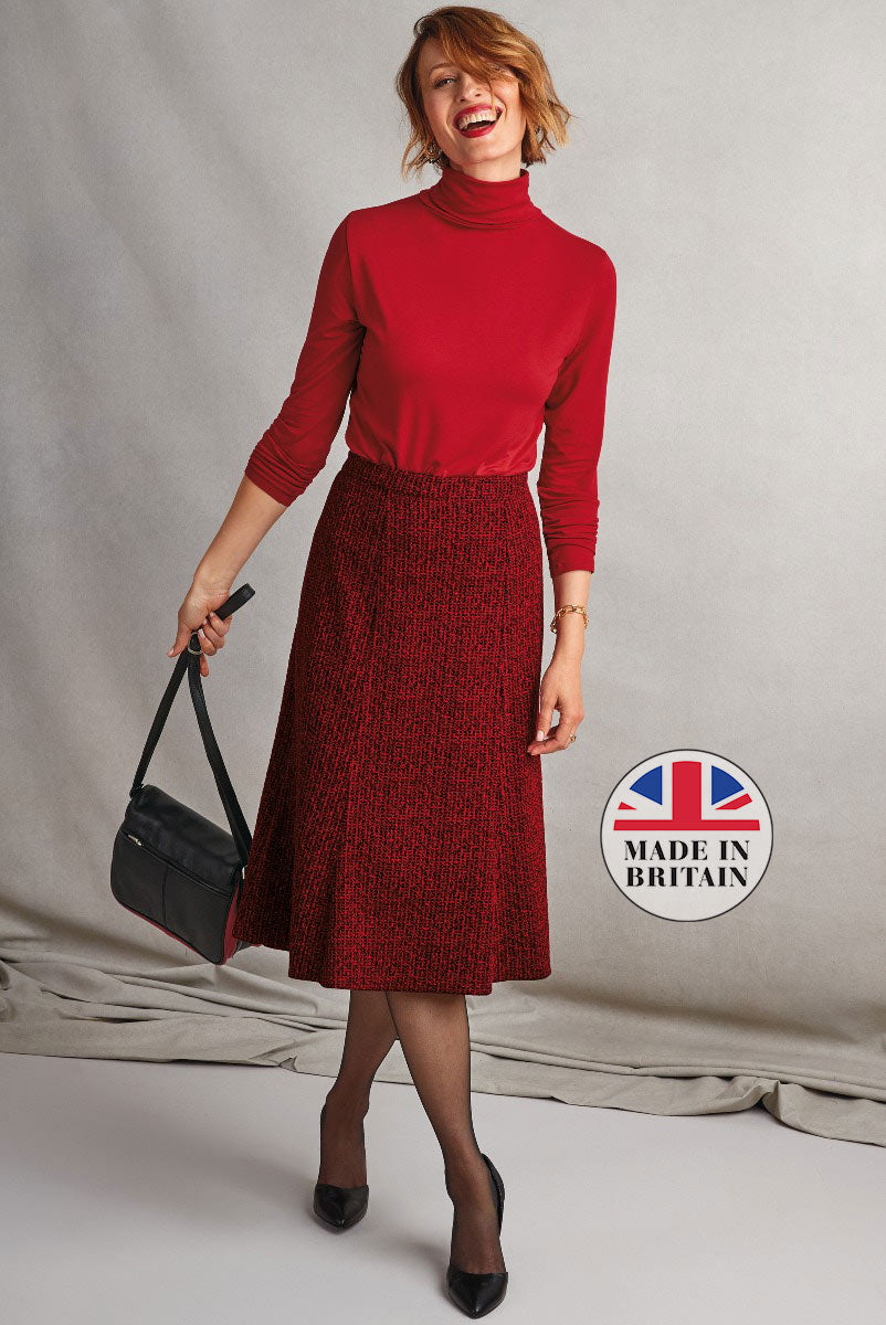 Lily Ella Collection autumn fashion - smiling woman in elegant red turtleneck and textured maroon A-line skirt with black shoulder bag and pumps, showcasing British-made women's clothing