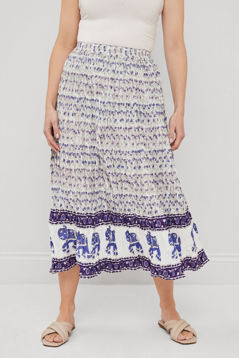 Lily Ella Collection printed mid-length skirt with pleats and contrasting hem in purple and white, paired with a beige top and sandals.