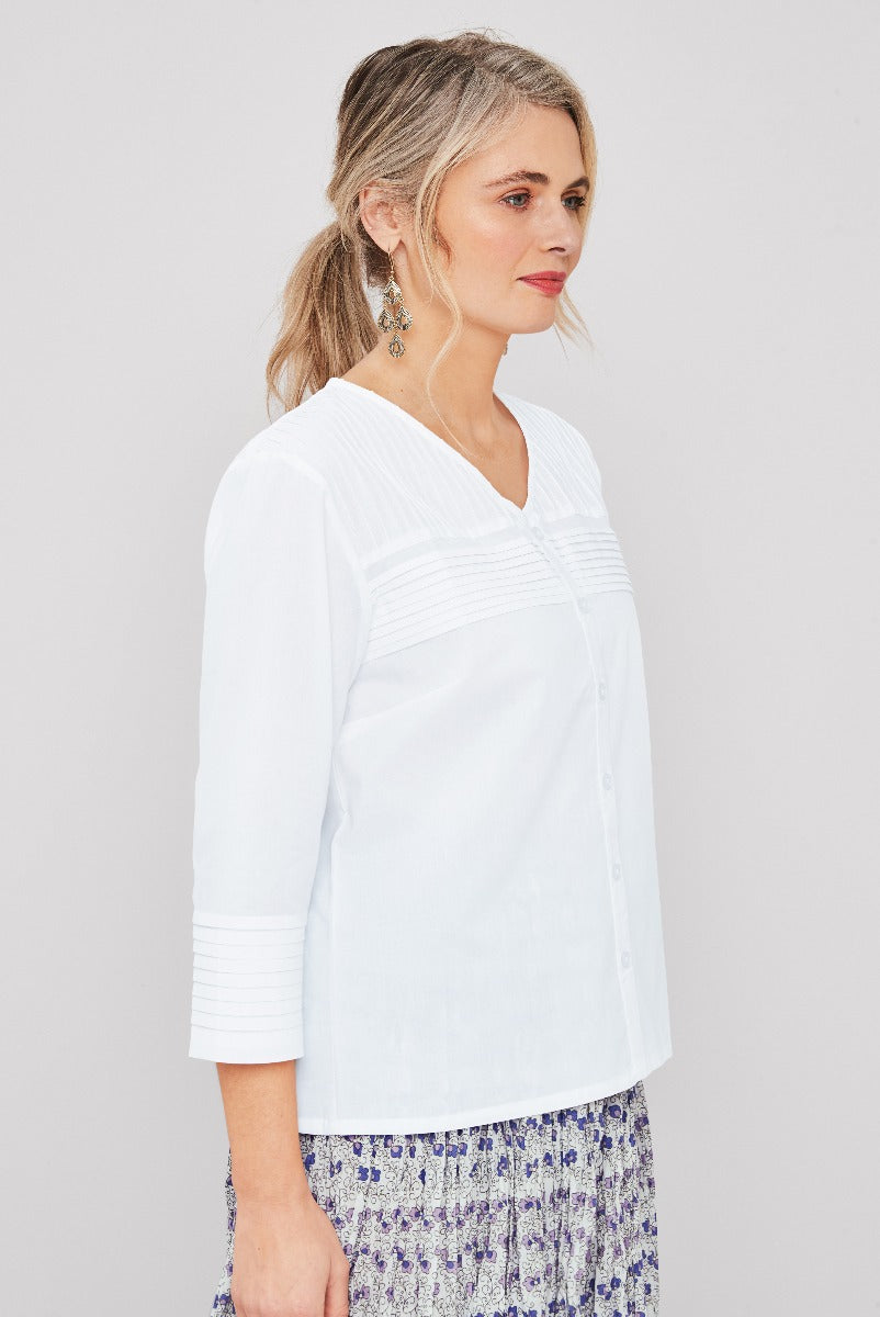 Lily Ella Collection white pintuck blouse with 3/4 sleeves styled with patterned skirt, elegant earrings and casual-chic makeup for fashion-forward women