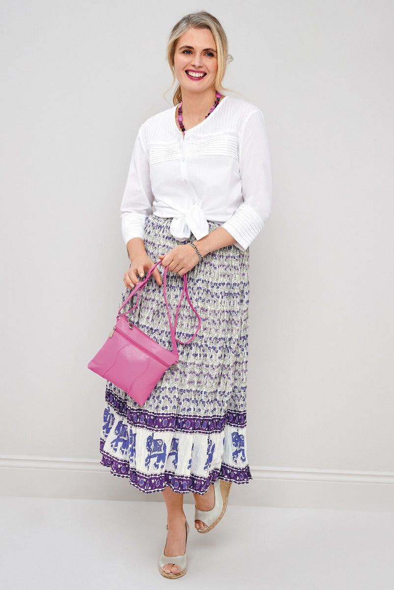 Lily Ella Collection white tie-front blouse and purple patterned maxi skirt with ruffle detail, accessorized with a pink shoulder bag and silver wedge sandals.