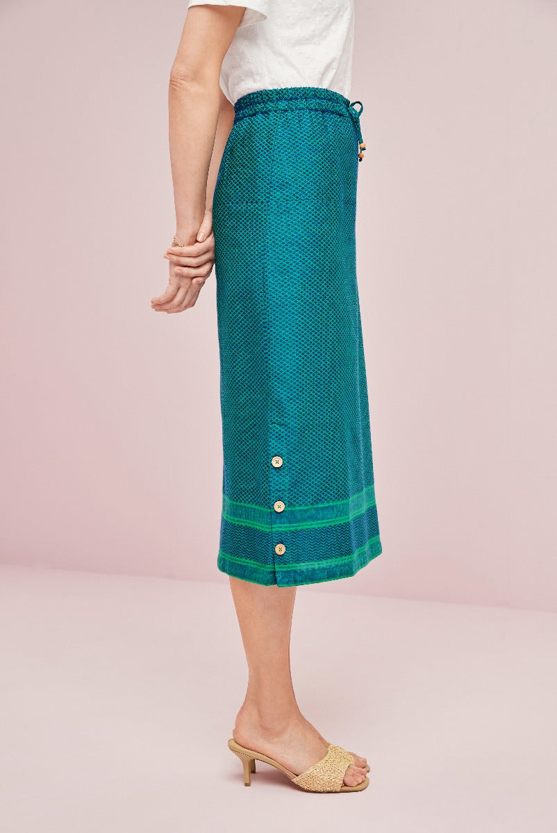 Lily Ella Collection teal green button-detail midi skirt with drawstring waistband paired with white tee and gold heeled sandals on pink background