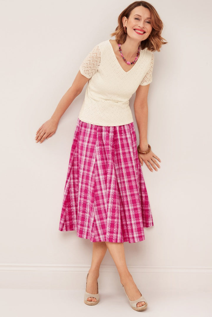 Lily Ella Collection fashion model wearing a textured cream knit top and vibrant pink plaid midi skirt with open-toe heels, accessorized with a purple beaded necklace.