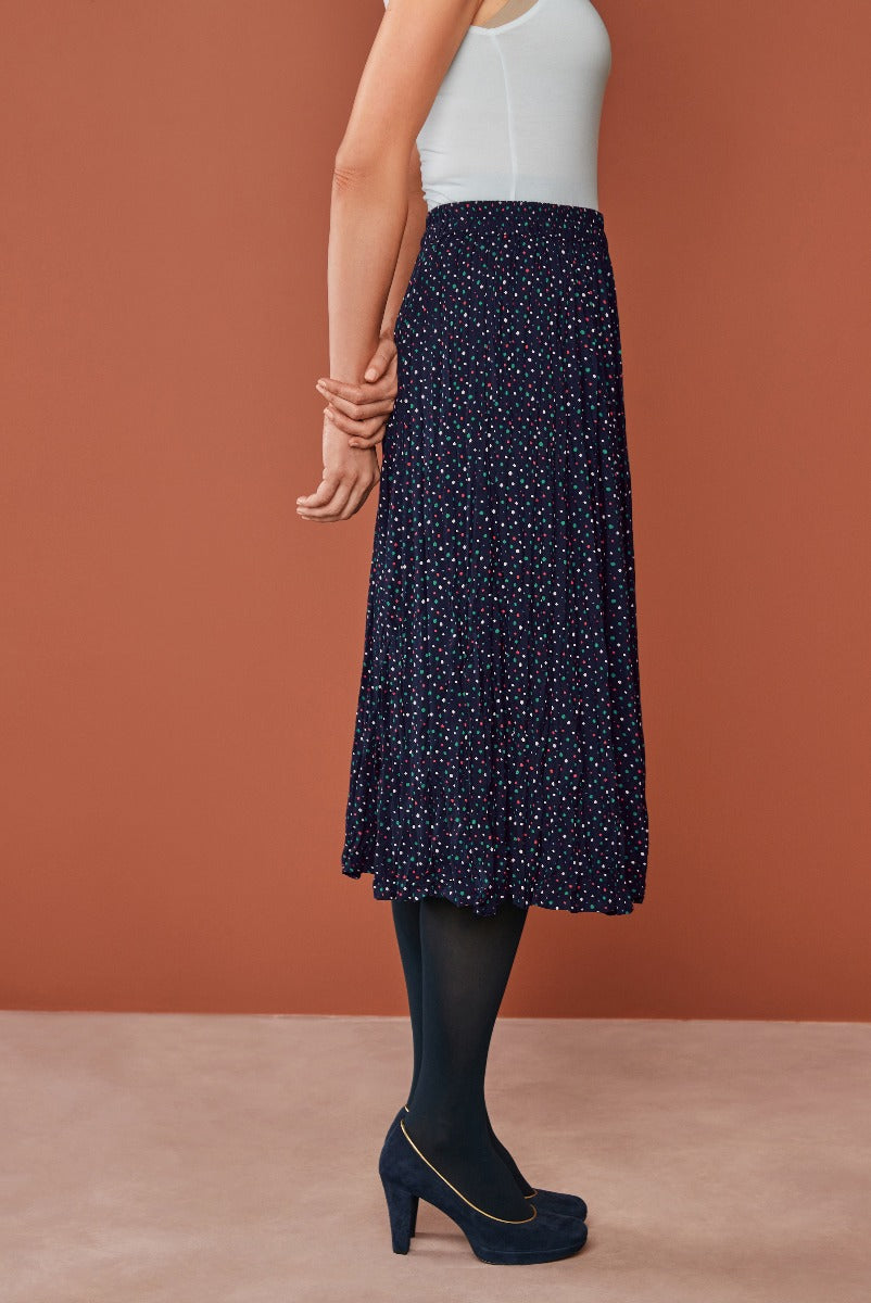 Lily Ella Collection women's mid-length navy skirt with colorful polka dots, paired with classic white top and black tights, elegant navy heels with gold accents, stylish and contemporary women's fashion.