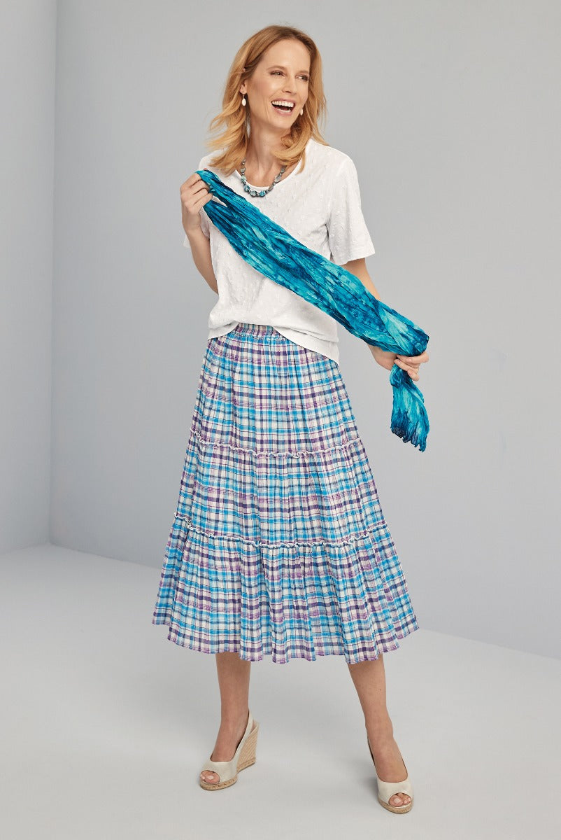 Lily Ella Collection vibrant blue scarf and plaid tiered skirt, stylish white top, model posing with joyful expression, elegant wedge sandals, modern women's fashion.