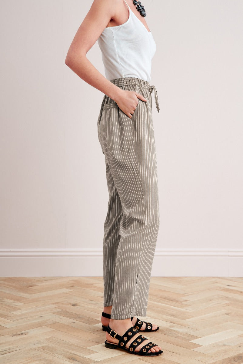 Lily Ella Collection striped beige linen trousers, casual summer style, woman wearing high-waisted pants with drawstring and sandal shoes, fashion-forward office wear, neutral-toned outfit