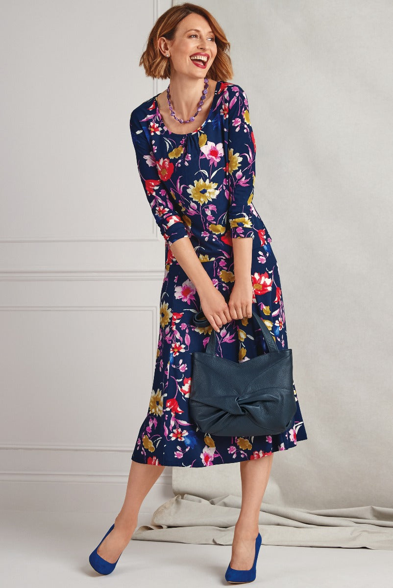 Lily Ella Collection stylish navy floral dress with coordinating blue accessories, featuring a smiling woman in a contemporary knee-length outfit perfect for spring and summer occasions