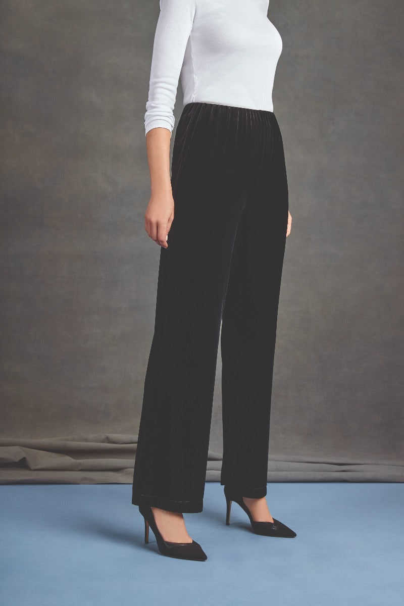 Lily Ella Collection elegant black velvet trousers with comfortable elastic waistband, paired with a white long-sleeve top and classic black heels, perfect for sophisticated evening wear.