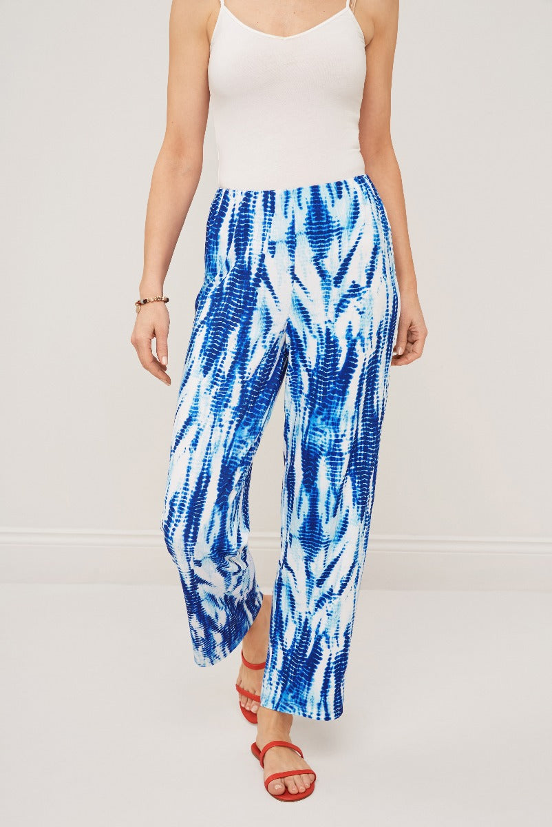 Lily Ella Collection blue and white tie-dye pattern palazzo pants for women, comfortable summer fashion, styled with white tank top and red sandals.