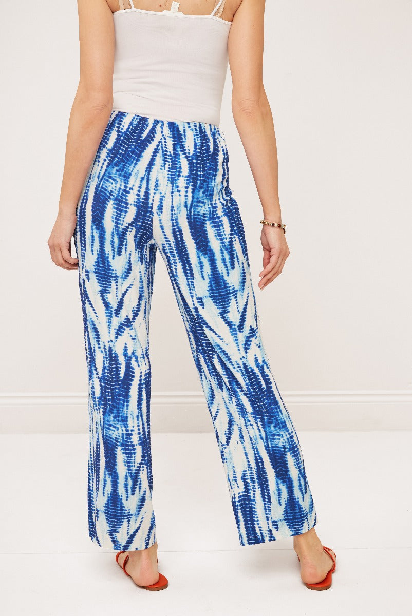 Lily Ella Collection blue and white tie-dye print trousers, stylish women's summer fashion pants, comfortable loose-fitting design, paired with casual white tank top and red sandals.