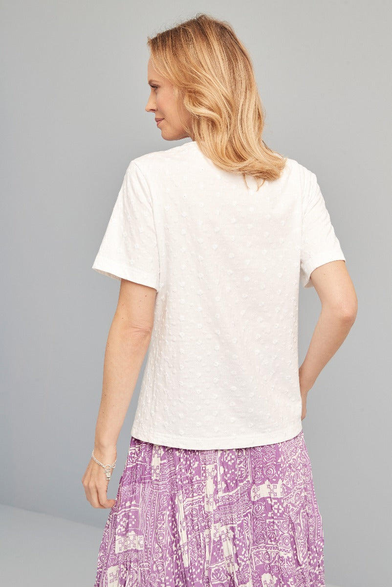 Lily Ella Collection white textured T-shirt paired with purple patterned skirt, women's casual summer outfit, back view