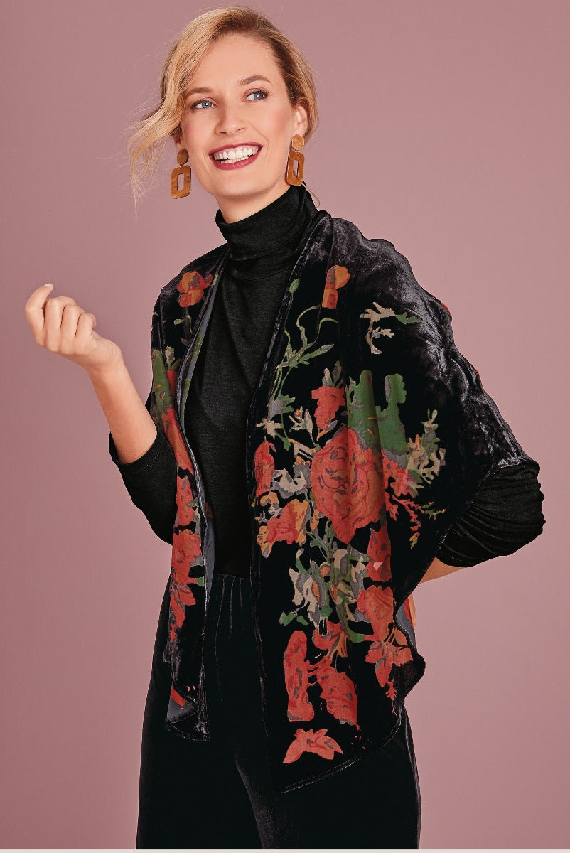 Lily Ella Collection floral velvet kimono in black with red and green pattern, stylish woman modeling trendy autumn outerwear with turtleneck and statement earrings.