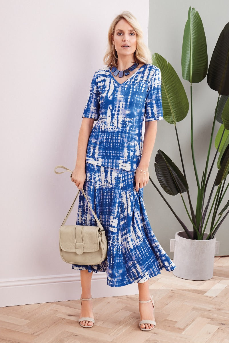 Lily Ella Collection blue and white tie-dye midi dress with a v-neck, model carrying beige shoulder bag and wearing beige sandals, stylish women's summer fashion.