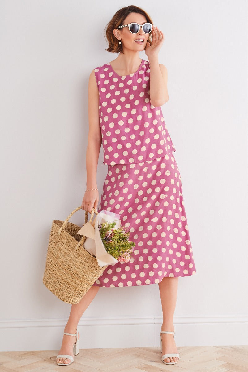 Lily Ella Collection polka dot sleeveless pink dress with matching layered top, stylish white sunglasses, straw tote bag with flowers, and white heeled sandals for summer fashion.