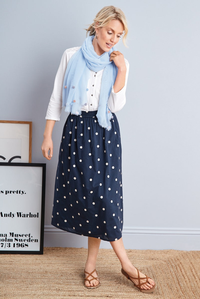 Lily Ella Collection navy blue polka dot midi skirt with white button-up cardigan and light blue frayed scarf, stylish summer outfit inspiration for women, casual elegant fashion look with tan strappy sandals