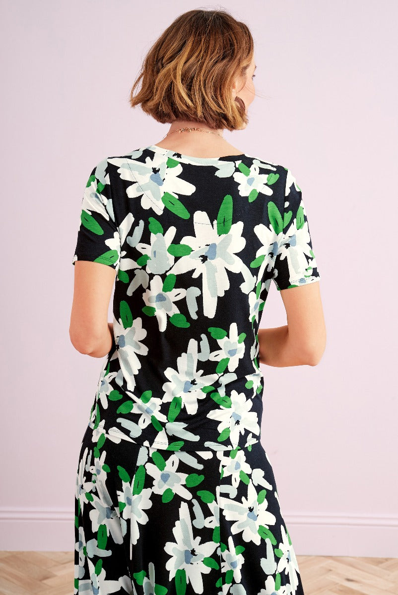 Lily Ella Collection black floral dress, woman modeling mid-length garment with white and green flower pattern, elegant casual wear, fashion, rear view.