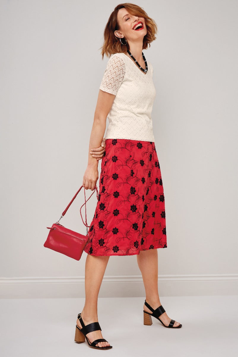 Lily Ella Collection stylish outfit featuring cream cable knit jumper and floral red midi skirt with black sandals and red handbag for a trendy spring look