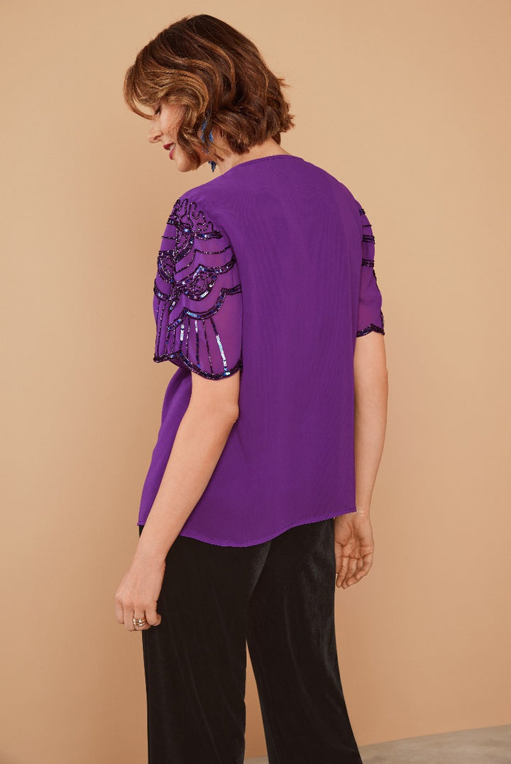 Lily Ella Collection purple blouse with embellished sequin detail, elegant short sleeves, and comfortable fit styled with black trousers for a sophisticated casual look.