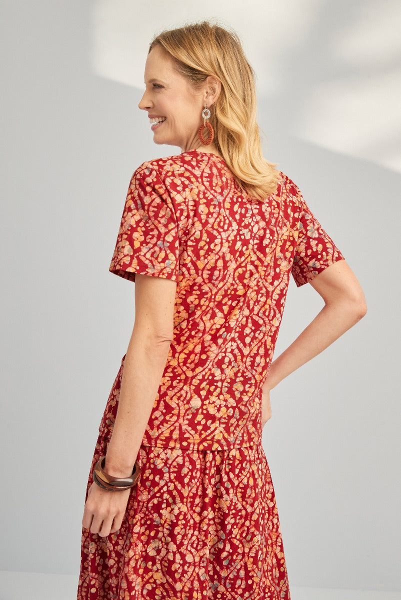 Lily Ella Collection red floral print dress, elegant short-sleeve A-line style, woman modeling spring/summer fashion with gold chandelier earrings and bracelets.