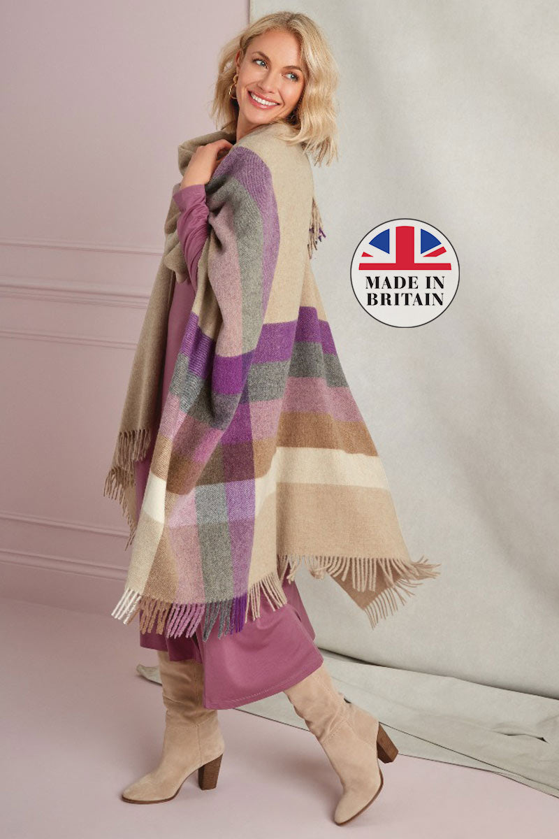 Lily Ella Collection Made in Britain - Woman wearing a beige, purple, and grey check patterned cape with tassel fringe over a mauve dress paired with beige knee-high boots.